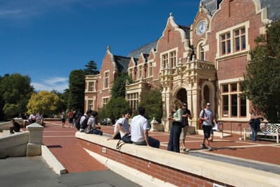 Barrierefreie Campuseinrichtungen in Neuseeland Studierende sitzen auf einer Mauer vor einem Unigebäude
